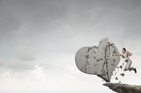 Young emotional woman in suit breaking stone heartの写真素材