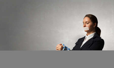 Young businesswoman with tape on mouth and tired handsの写真素材