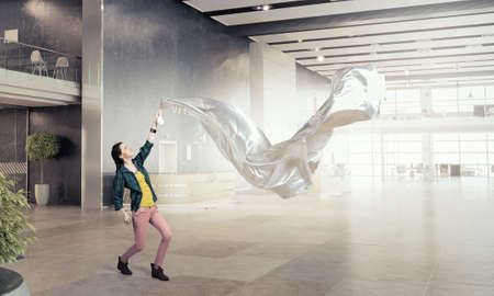 Young woman in office interior pulling white blank fabricの写真素材