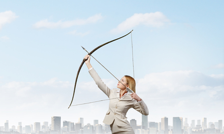 Young businesswoman aiming with archer to make shotの写真素材