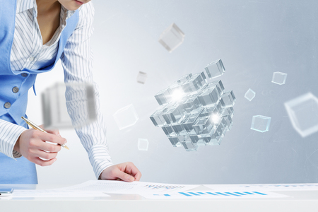 Close view of businesswoman writing on papers and 3D illustration cube figure as technology conceptの写真素材