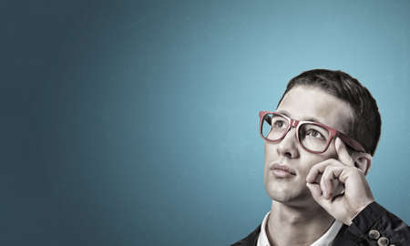 Young man in red glasses and jacket looking thoughtfully up