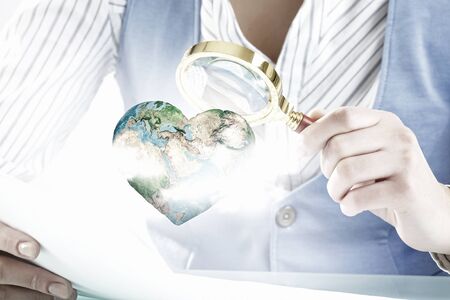 Close view of businesswoman examining Earth planet with magnifying glass.の写真素材