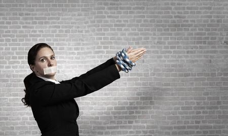 Young businesswoman with tape on mouth and tired handsの写真素材