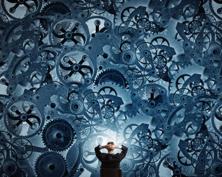 Young relaxed businessman sitting in chair and looking at gears mechanismの写真素材