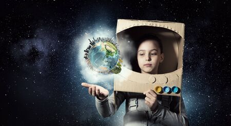 Cute kid girl with carton helmet on head dreaming to become astronaut.