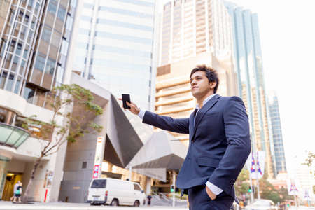 Businessman in suit catching taxi in city with mobile phone in his handsの写真素材