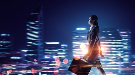Young elegant businesswoman against night city backgroundの写真素材