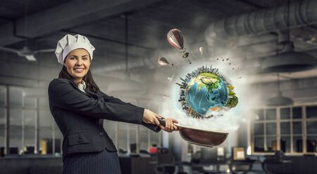 Pretty businesswoman in suit and cook hat with pan in hand. Elements of this image are furnished by NASAの写真素材