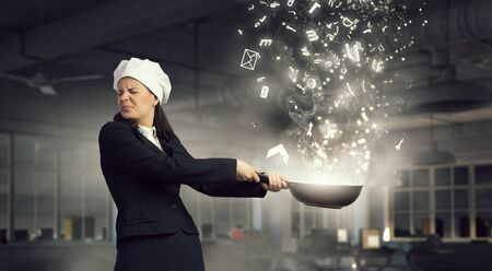 Pretty businesswoman in suit and cook hat with pan in handの写真素材