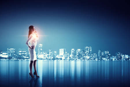 Young businesswoman with mobile phone against night city backgroundの写真素材
