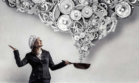 Pretty businesswoman in suit and cook hat with pan in handの写真素材