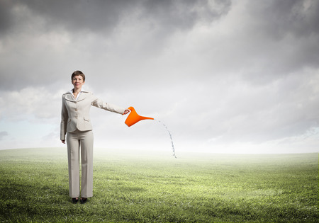 Young businesswoman watering green plant with canの写真素材
