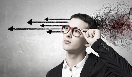 Thoughtful businessman with arrows and thoughts coming out of his headの写真素材