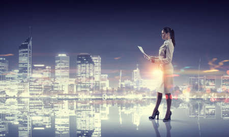 Young elegant businesswoman against night city backgroundの写真素材