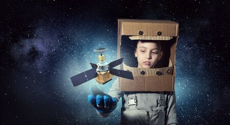 Cute kid girl with carton helmet on head dreaming to become astronautの写真素材