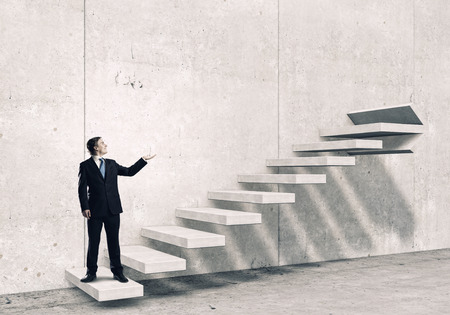 Young businessman reaching up staircase as symbol of growth and progressの写真素材