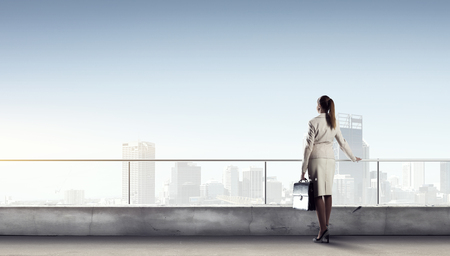 Young elegant businesswoman on roof looking at cityの写真素材
