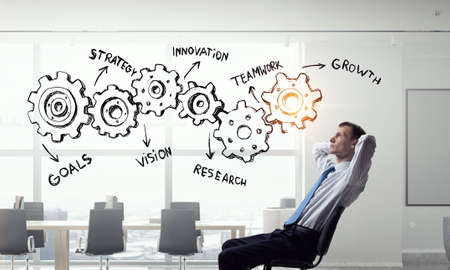 Relaxed businessman at the office sitting back with his hands behind his headの写真素材