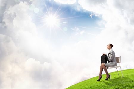 Young pretty businesswoman sitting on chair with briefcase in handsの写真素材