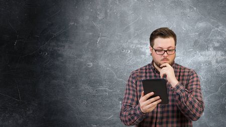 Young thoughtful man in checked shirt using tablet pcの写真素材