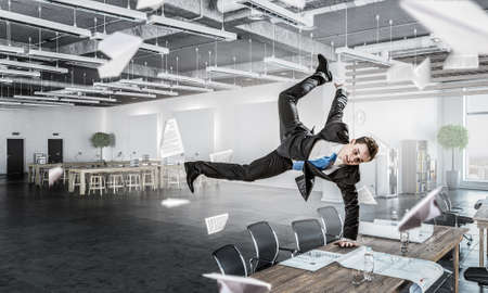 Youngh cheerful businessman dancing in office. Mixed media