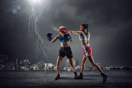 Two young pretty women boxing against night city backgroundの写真素材