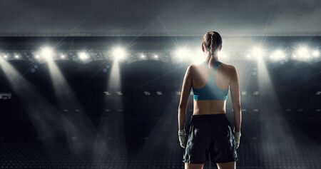 Young pretty boxer woman standing in lights of sport arenaの写真素材