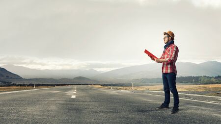 Hipster guy with book in hands on asphalt roadの写真素材
