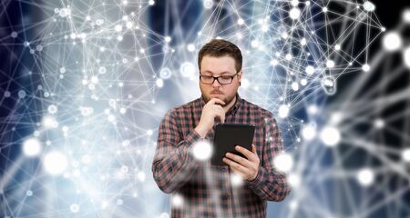 Young thoughtful man in checked shirt using tablet pcの写真素材