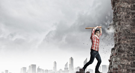 Furious hipster guy breaking wall with baseball batの写真素材