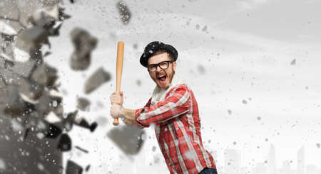 Furious hipster guy breaking wall with baseball batの写真素材