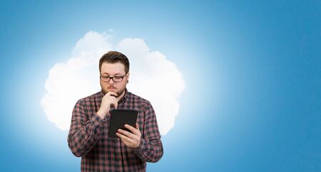 Young thoughtful man in checked shirt using tablet pcの写真素材