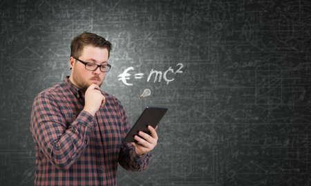 Young thoughtful man in checked shirt using tablet pc