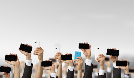 Group of people with hands up showing mobile phonesの写真素材