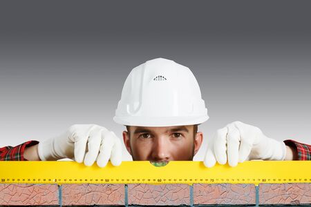Bricklayer using level to check new red brick wall outdoor