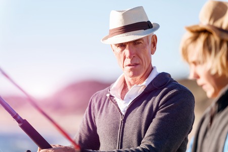 Senior man fishing with his teenage grandson at seaside