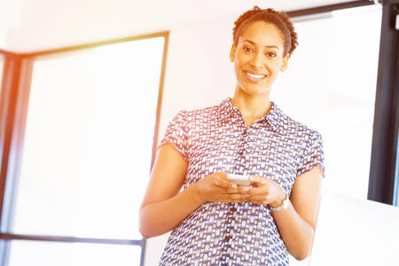 Portrait of beautiful smiling afro-american office worker in office with her mobile phones