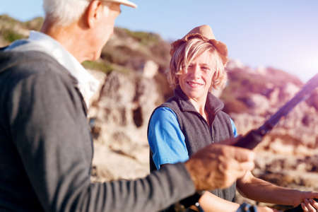 Senior man fishing with his teenage grandson at seaside