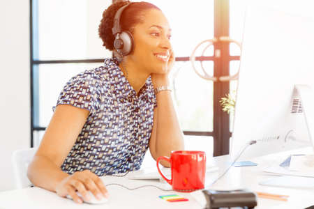 Portrait of beautiful smiling afro-american office worker sitting in office with headphonesの写真素材