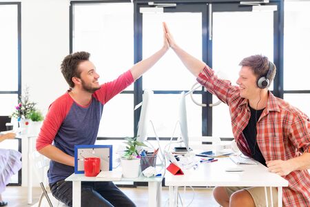 Two young man in office clapping their hands as symbol of victory