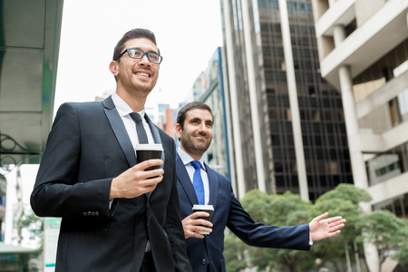 Two young businessmen in suits catching taxiの写真素材