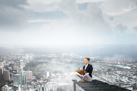 Back view of businesswoman sitting on bay and reading bookの写真素材