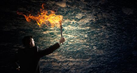 Young businessman in darkness holding burning torch in handの写真素材