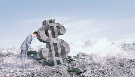 Young businessman with suitcase leaning head to big dollar signの写真素材