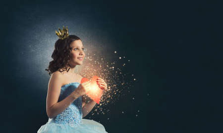Little cute princess in dress and crown with heart in handsの写真素材