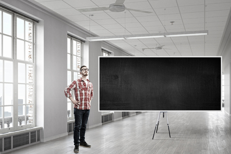 Young man in glasses and checked shirt in room with blackboard. Mixed mediaの写真素材