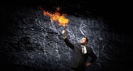 Young businessman in darkness holding burning torch in handの写真素材