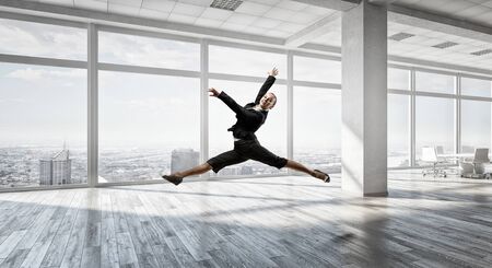 Young cheerful businesswoman in modern office interior dancing like ballerina. Mixed mediaの写真素材