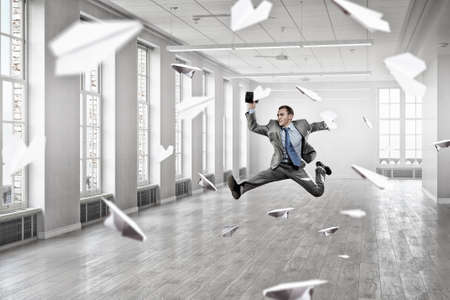 Cheerful businessman in office interior jumping high. Mixed media